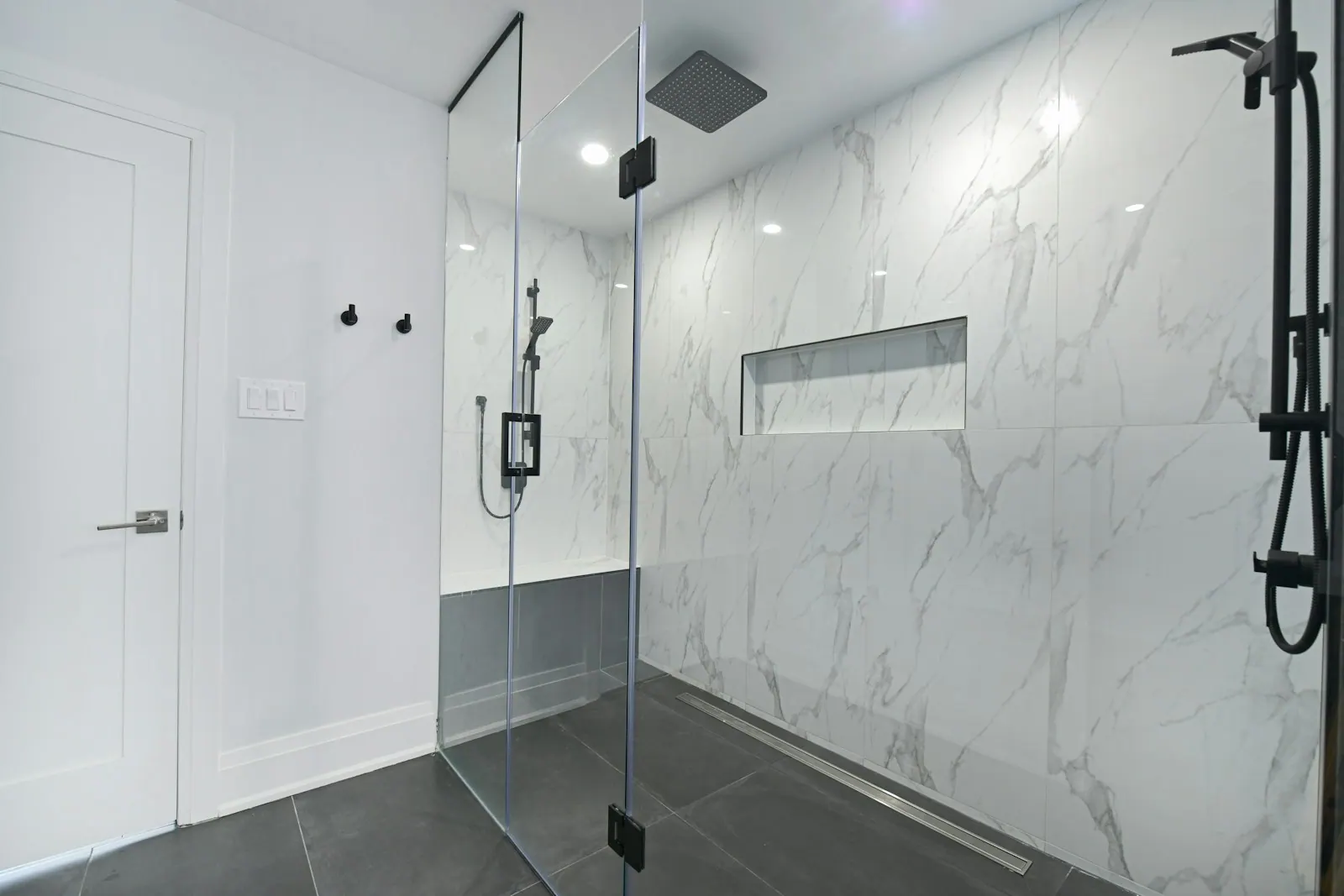 Modern bathroom renovation with a glass walk-in shower and marble walls